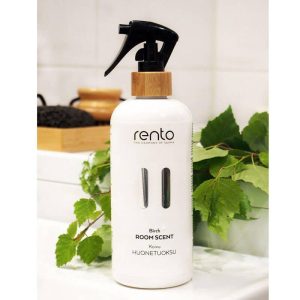 White bottle of Rento birch room scent with a black spray nozzle, surrounded by green leaves on a white surface.