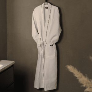 A white bathrobe hangs on a hook against a plain wall. Nearby, a countertop with a sink is partially visible.
