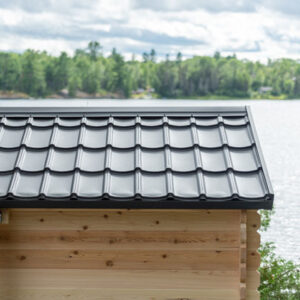 A wooden structure with a dark, tiled roof by a serene lake, surrounded by lush green forest under a cloudy sky.